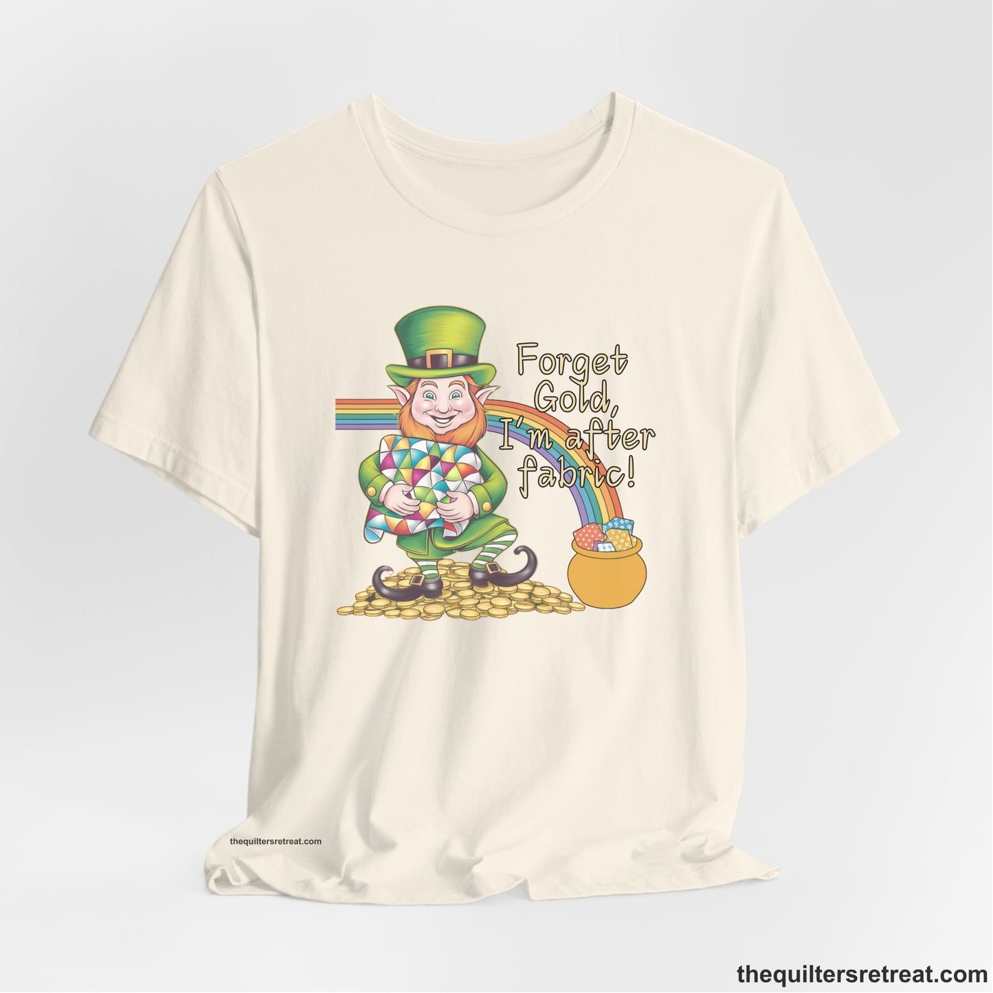 A Natural Short Sleeve T-Shirt with a leprechaun with colorful quilt and rainbow, whimsical "Forget Gold, I'm after fabric!" text