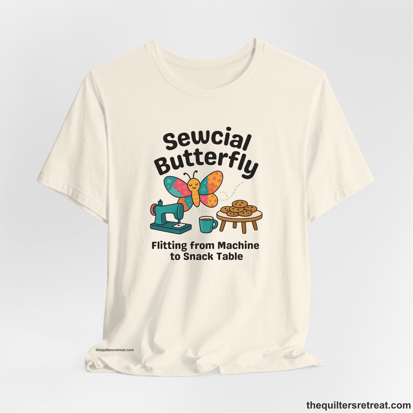A Natural Short Sleeve T-Shirt with a playful butterfly near sewing machine with cookies and coffee doodle design