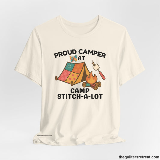 A Natural Short Sleeve T-Shirt with a camping scene with patchwork tent, campfire, and whimsical butterfly and marshmallow illustration