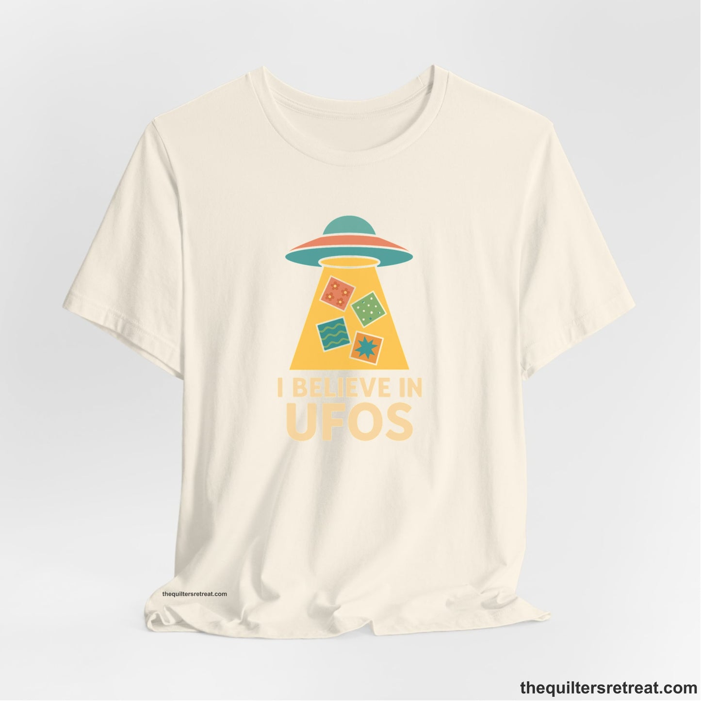 A Natural Short Sleeve T-Shirt with a colorful UFO with quilt patterns and bold "I Believe in UFOs" text in retro style