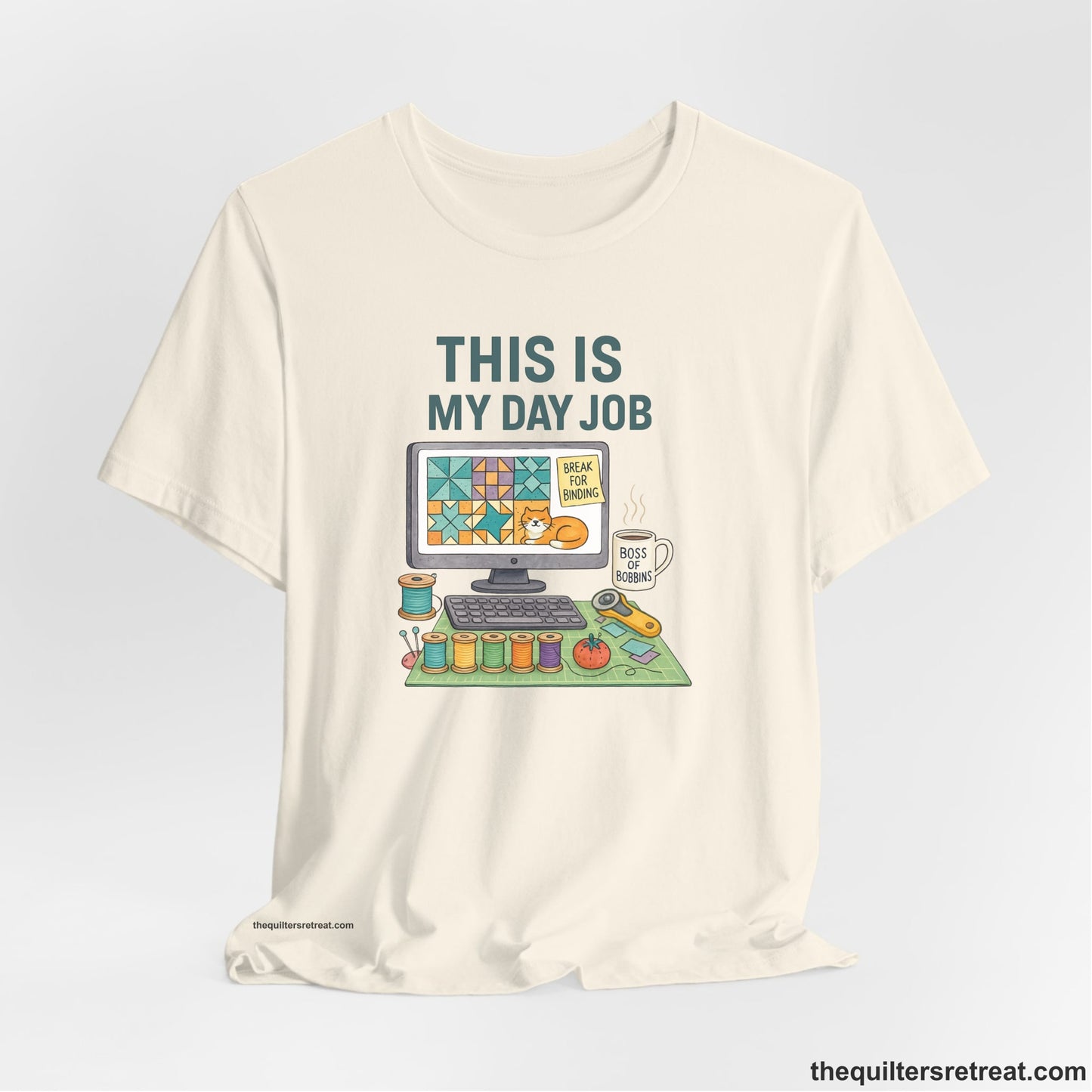 A Natural Short Sleeve T-Shirt with a computer quilt design, cat illustration, "THIS IS MY DAY JOB" text with sewing tools, playful style