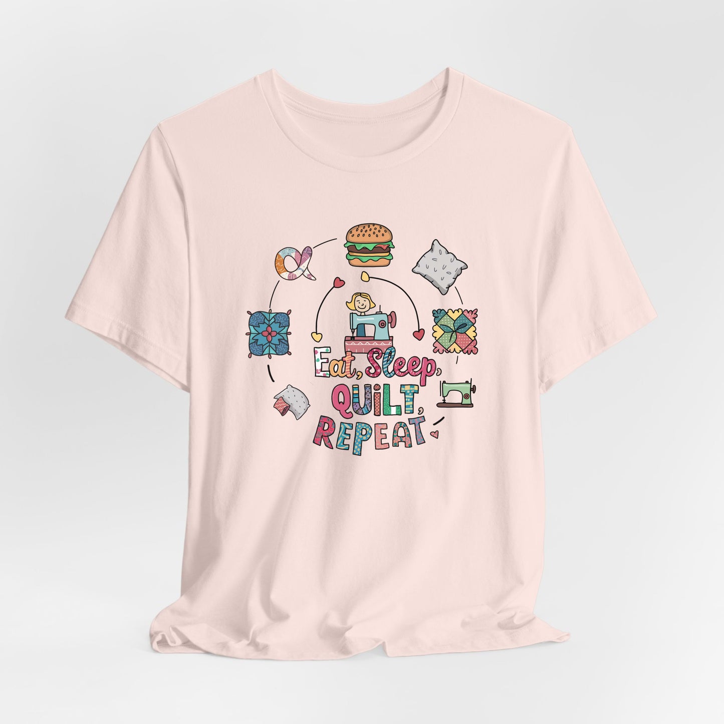 A Soft Pink Short Sleeve T-Shirt with a cute quilting elements with "Eat, Sleep, Quilt, Repeat" text in playful style