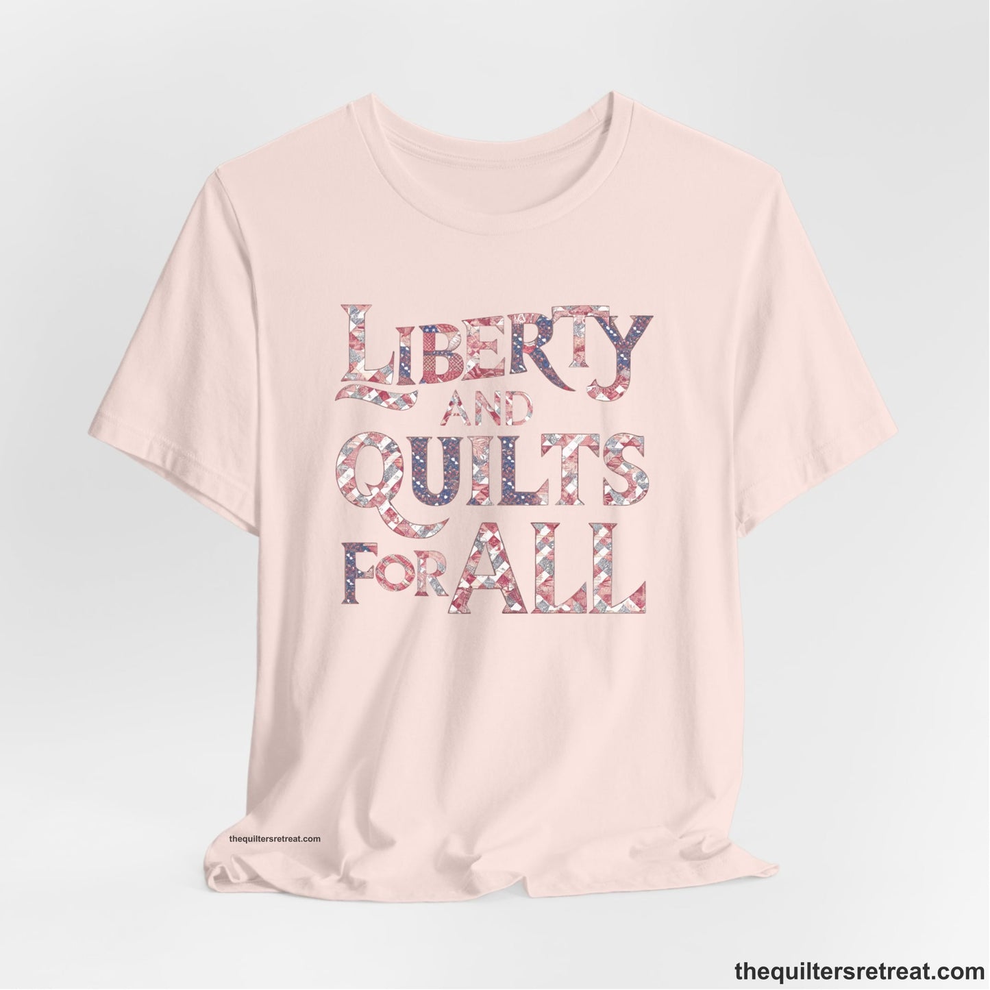 A Soft Pink Short Sleeve T-Shirt with a Liberty and Quilts for All" text with patchwork quilt pattern in a vintage style