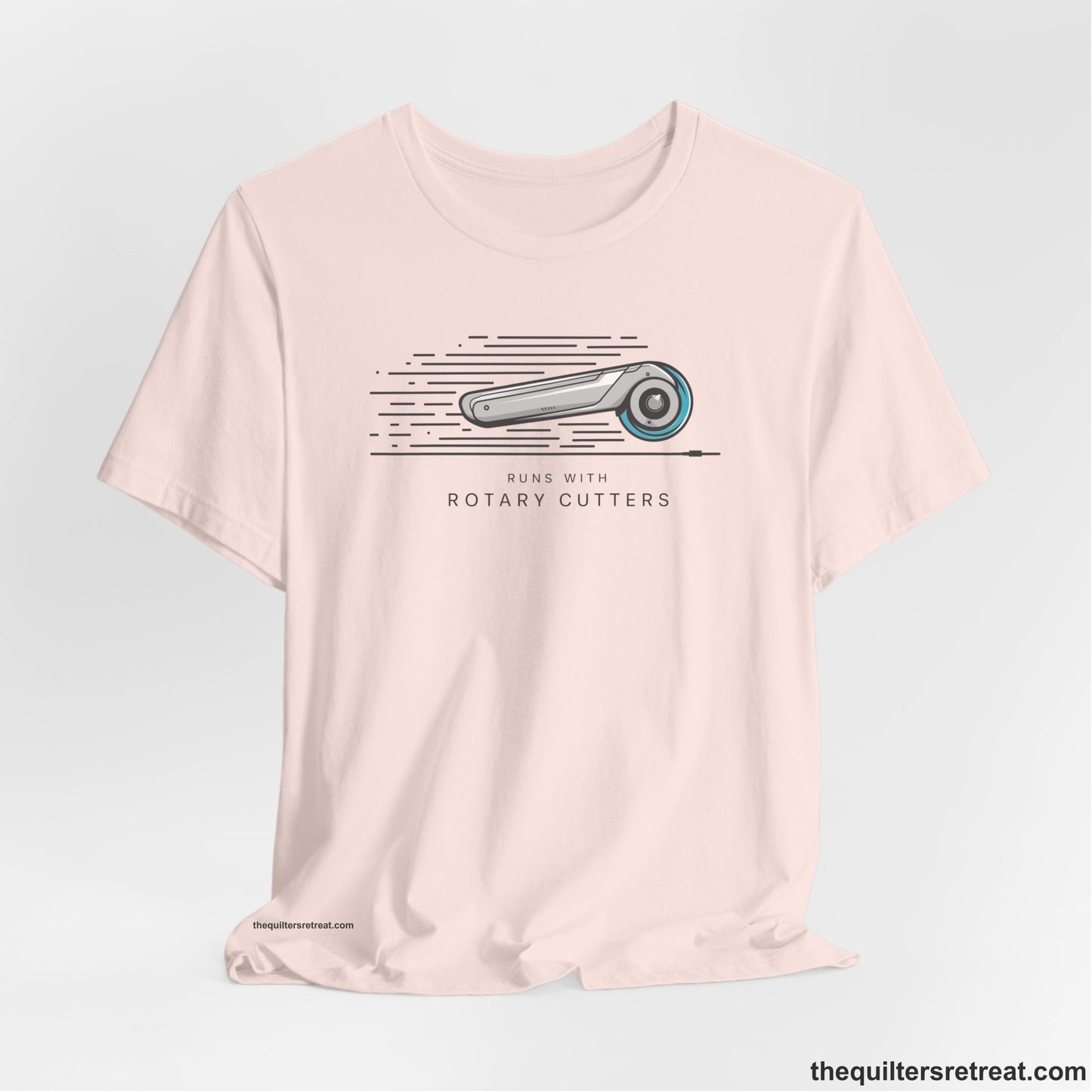 A Soft Pink Short Sleeve T-Shirt with a rotary cutter illustration with dynamic lines and bold "Runs with Rotary Cutters" text