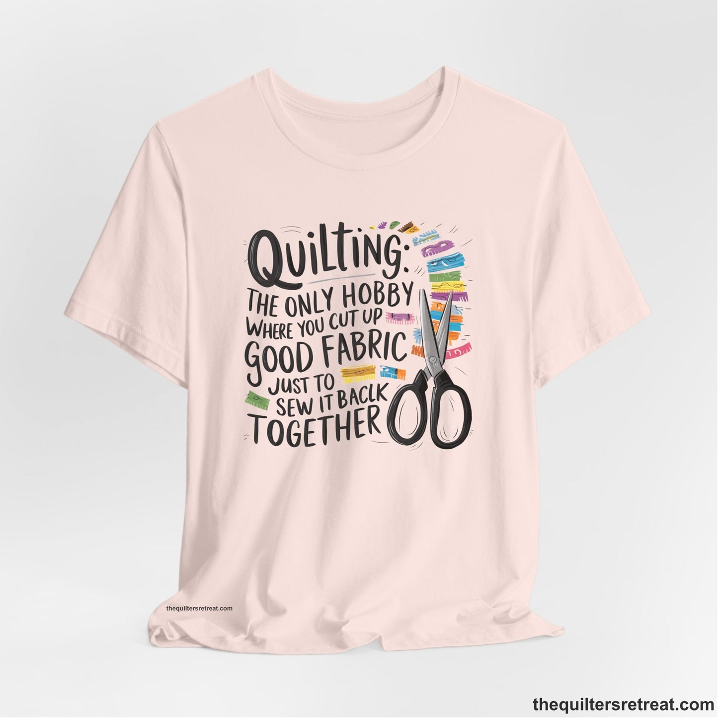 A Soft Pink Short Sleeve T-Shirt with a quilting-themed text with colorful fabric pieces and scissors in a whimsical style