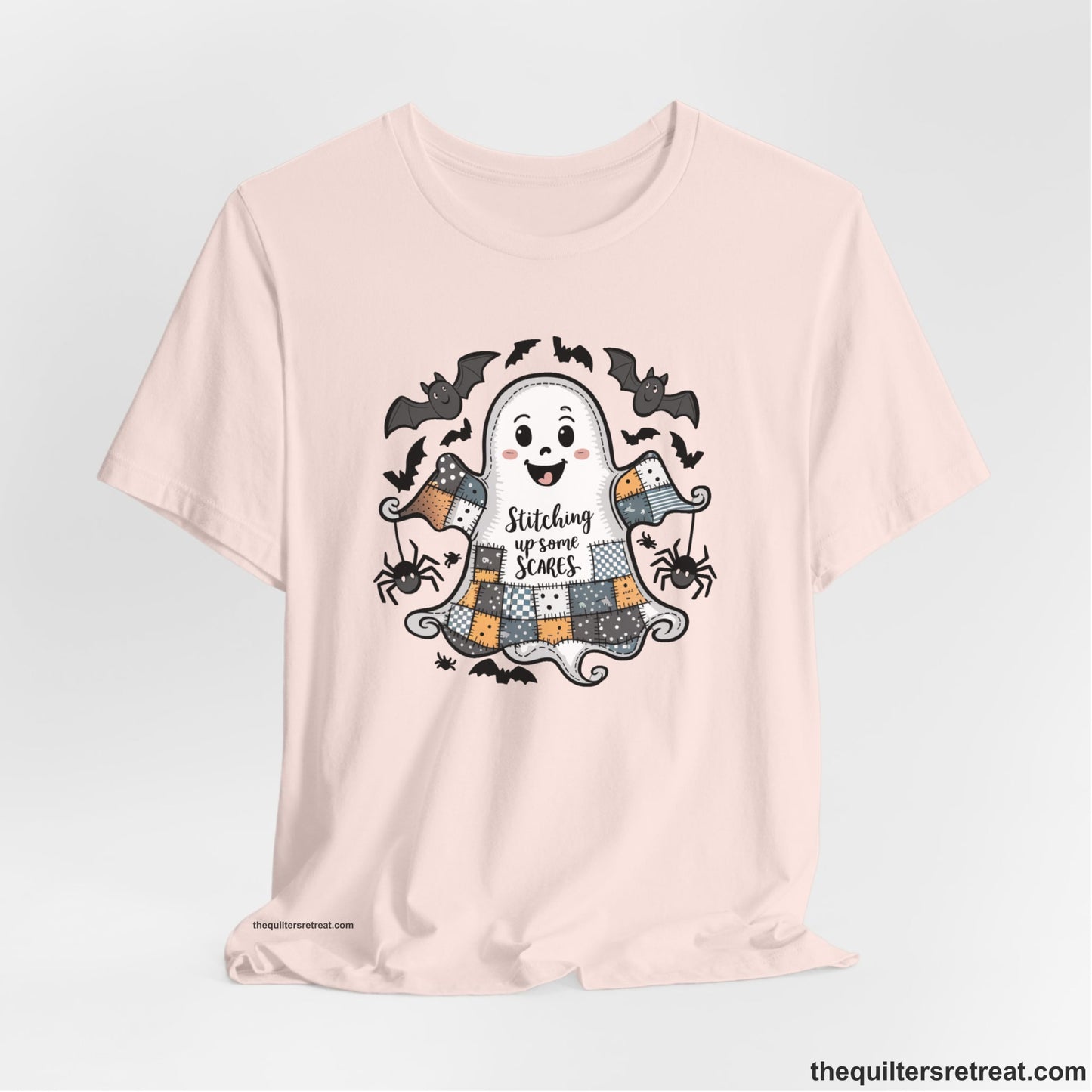 A Soft Pink Short Sleeve T-Shirt with a cute patchwork ghost with "Stitching up some Scares" text and playful bats in a whimsical style