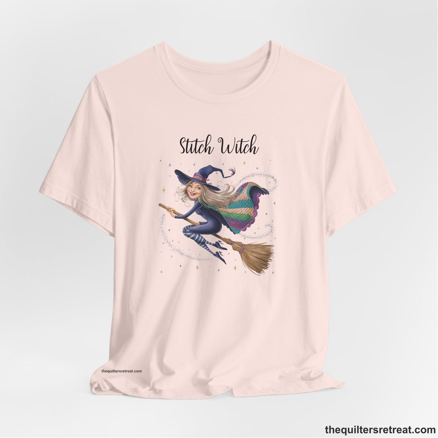A Soft Pink Short Sleeve T-Shirt with a playful witch on broomstick with patchwork cape and starry background in a whimsical style