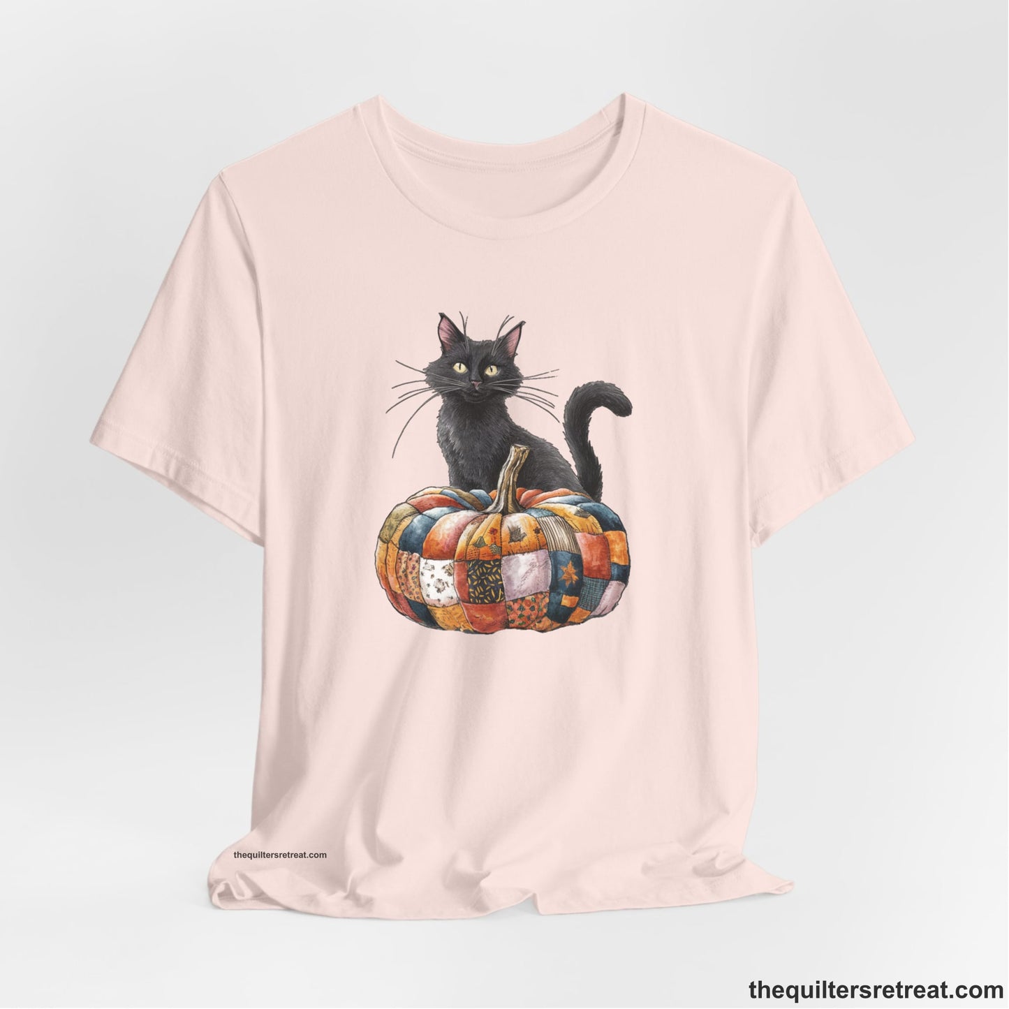 A Soft Pink Short Sleeve T-Shirt with a black cat with a quilted patchwork pumpkin in a whimsical autumn style