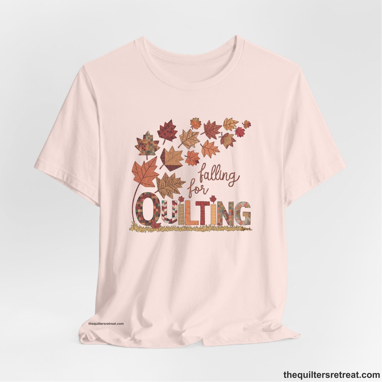 A Soft Pink Short Sleeve T-Shirt with a falling autumn leaves and "Falling for Quilting" text in a patchwork style