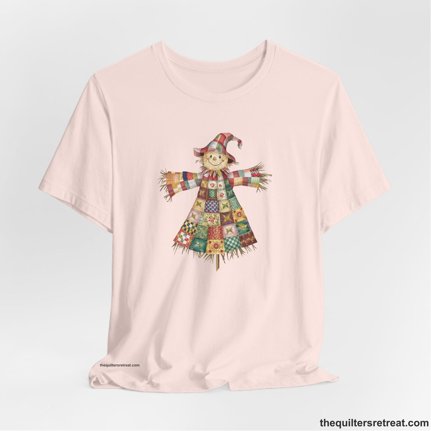 A Soft Pink Short Sleeve T-Shirt with a patchwork scarecrow with a cheerful face in a whimsical style