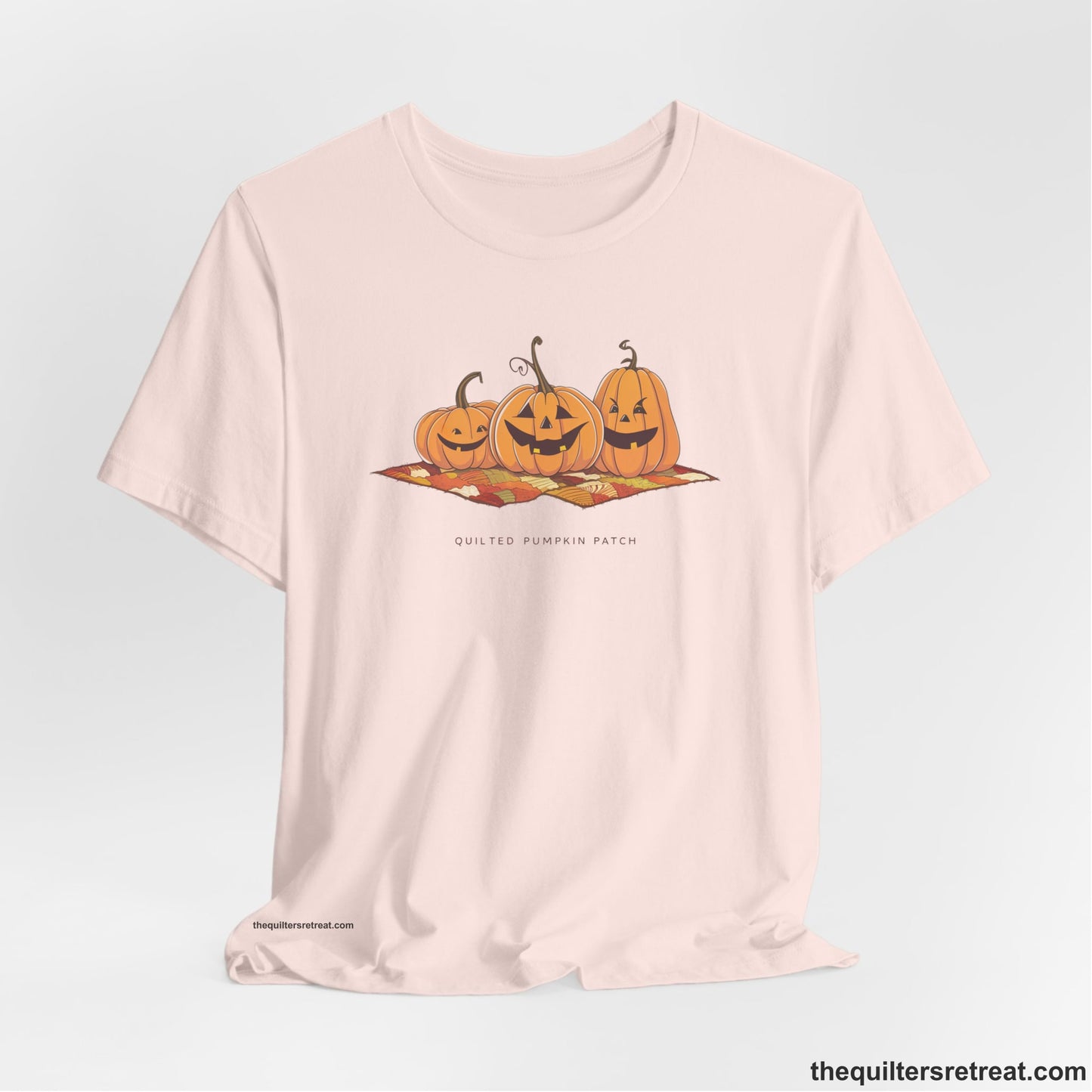 A Soft Pink Short Sleeve T-Shirt with a playful jack-o'-lantern trio on a quilt with "Quilted Pumpkin Patch" text