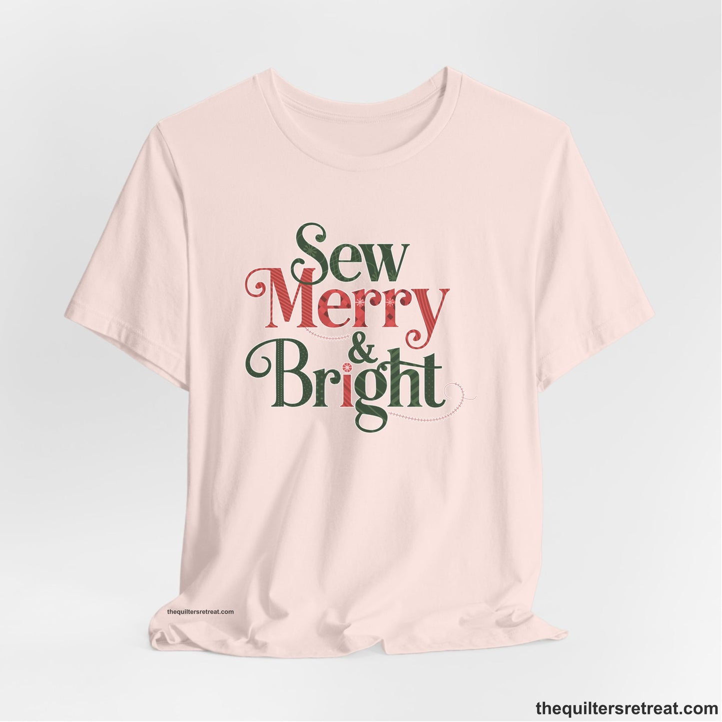 A Soft Pink Short Sleeve T-Shirt with a festive "Sew Merry & Bright" text with decorative holiday patterns