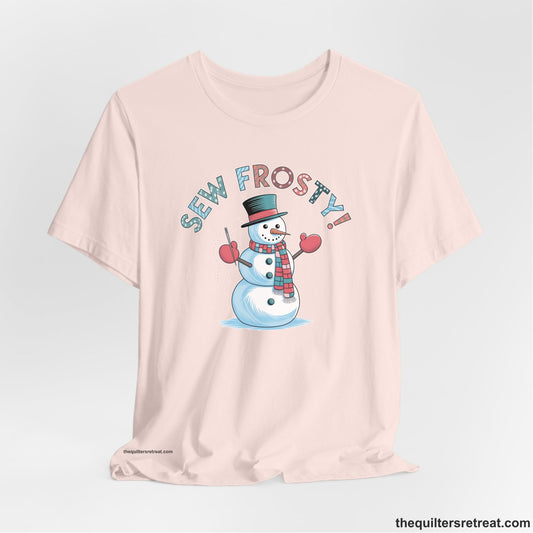 A Soft Pink Short Sleeve T-Shirt with a playful snowman sewing illustration with "Sew Frosty!" text in a festive style