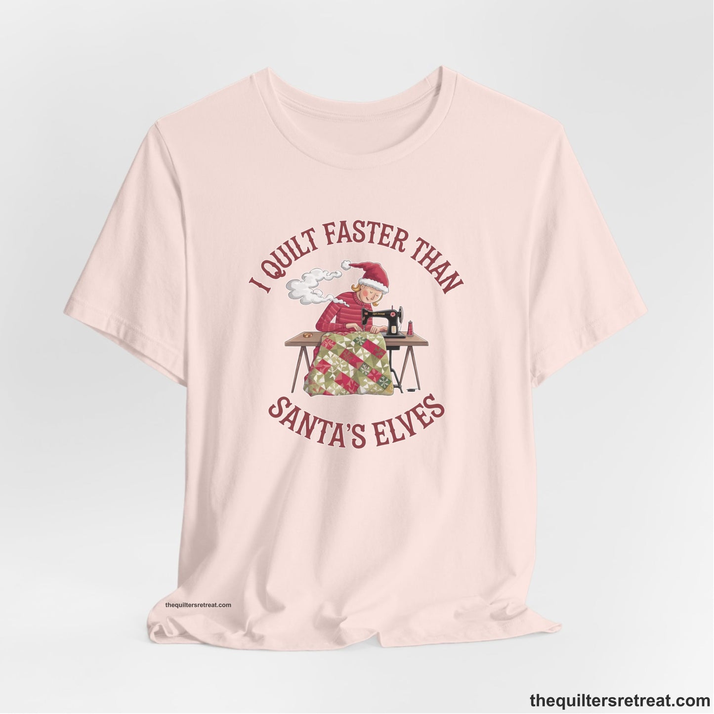 A Soft Pink Short Sleeve T-Shirt with a whimsical illustration of a quilting woman with "I Quilt Faster Than Santa's Elves" text
