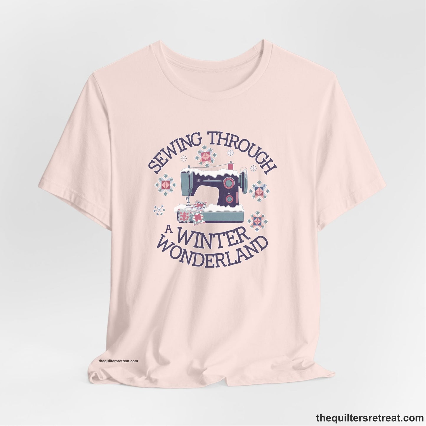 A Soft Pink Short Sleeve T-Shirt with a sewing machine covered in snow with festive quilting elements and "Sewing Through a Winter Wonderland" text
