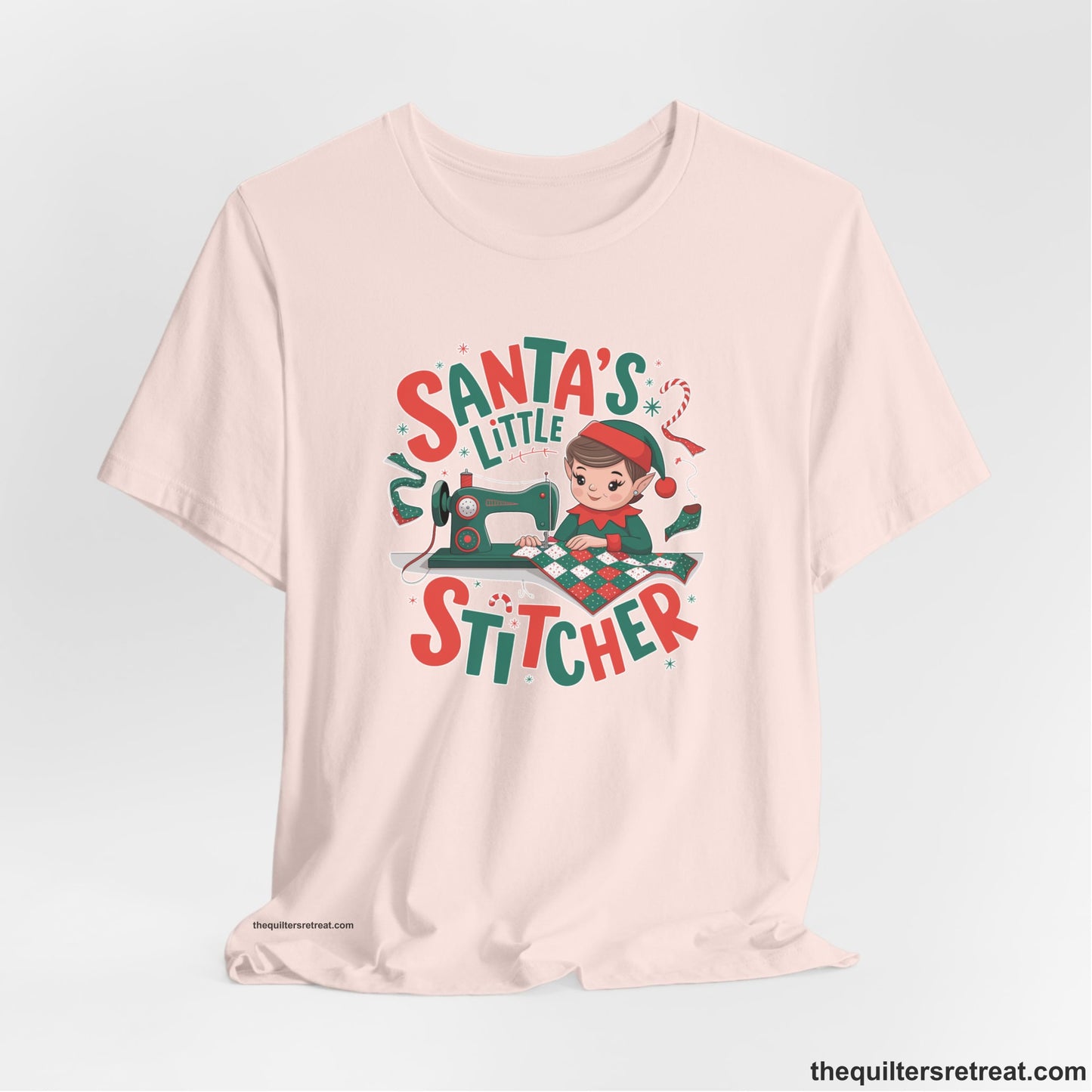 A Soft Pink Short Sleeve T-Shirt with a santa's little stitcher elf sewing quilt with festive colors in playful style