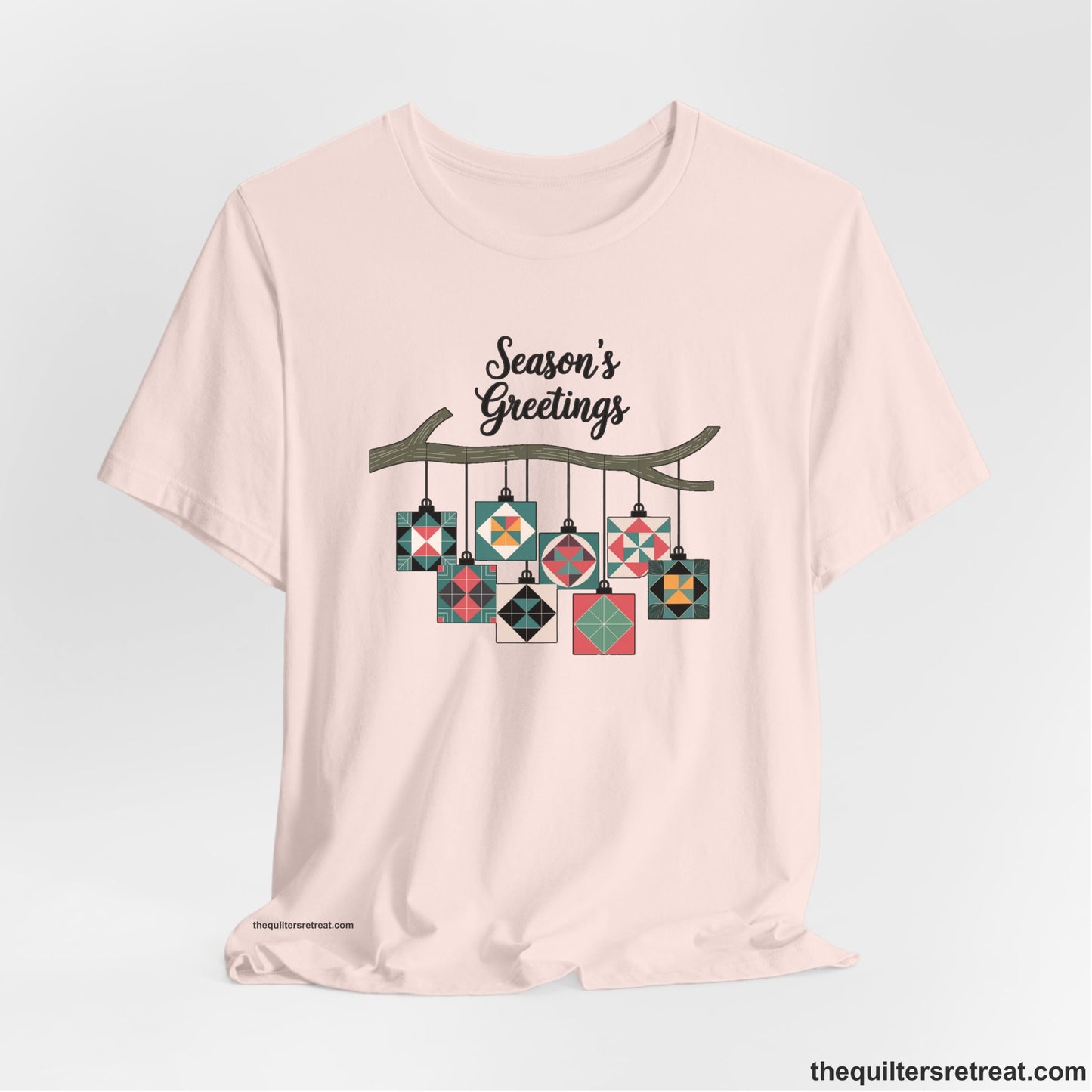 A Soft Pink Short Sleeve T-Shirt with a season's greetings text above colorful quilt block ornaments on tree branch in rustic style
