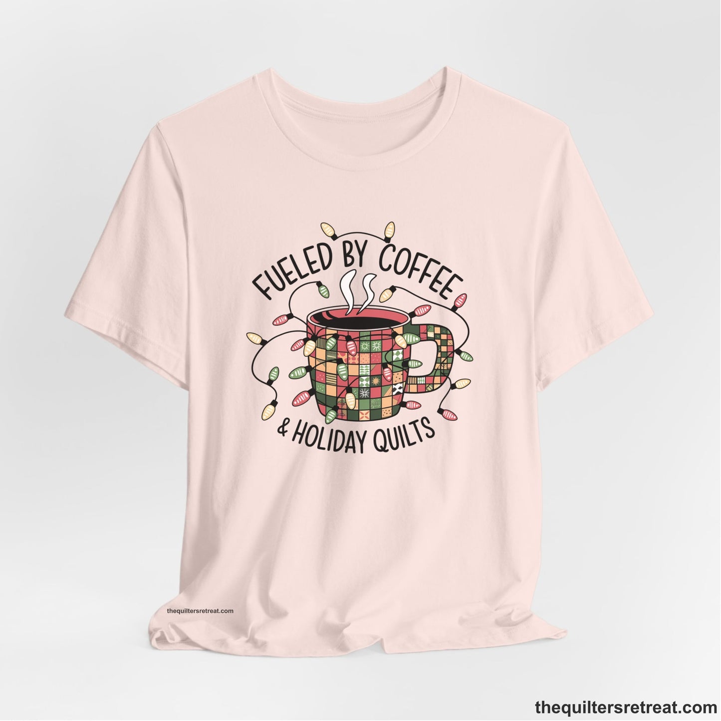 A Soft Pink Short Sleeve T-Shirt with a patchwork coffee mug with colorful lights and subtle "Fueled by Coffee" text in festive style