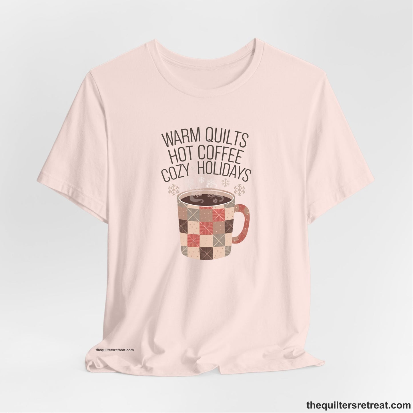 A Soft Pink Short Sleeve T-Shirt with a warm quilts hot coffee cozy holidays text with a patchwork mug and snowflakes