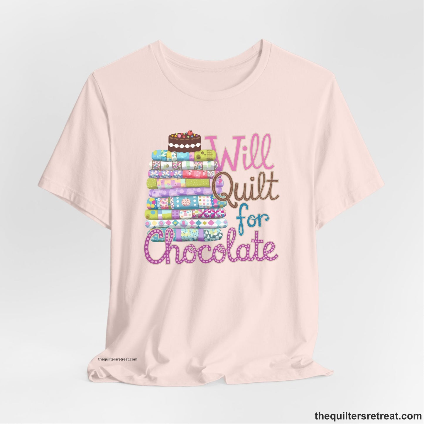 A Soft Pink Short Sleeve T-Shirt with a stack of colorful quilts topped with cake, whimsical "Will Quilt for Chocolate" text