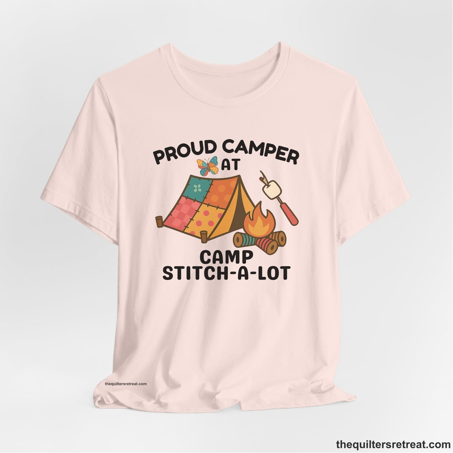 A Soft Pink Short Sleeve T-Shirt with a camping scene with patchwork tent, campfire, and whimsical butterfly and marshmallow illustration