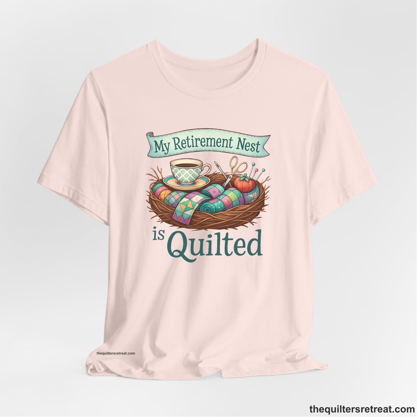 A Soft Pink Short Sleeve T-Shirt with a My Retirement Nest is Quilted text with a cozy sewing elements illustration