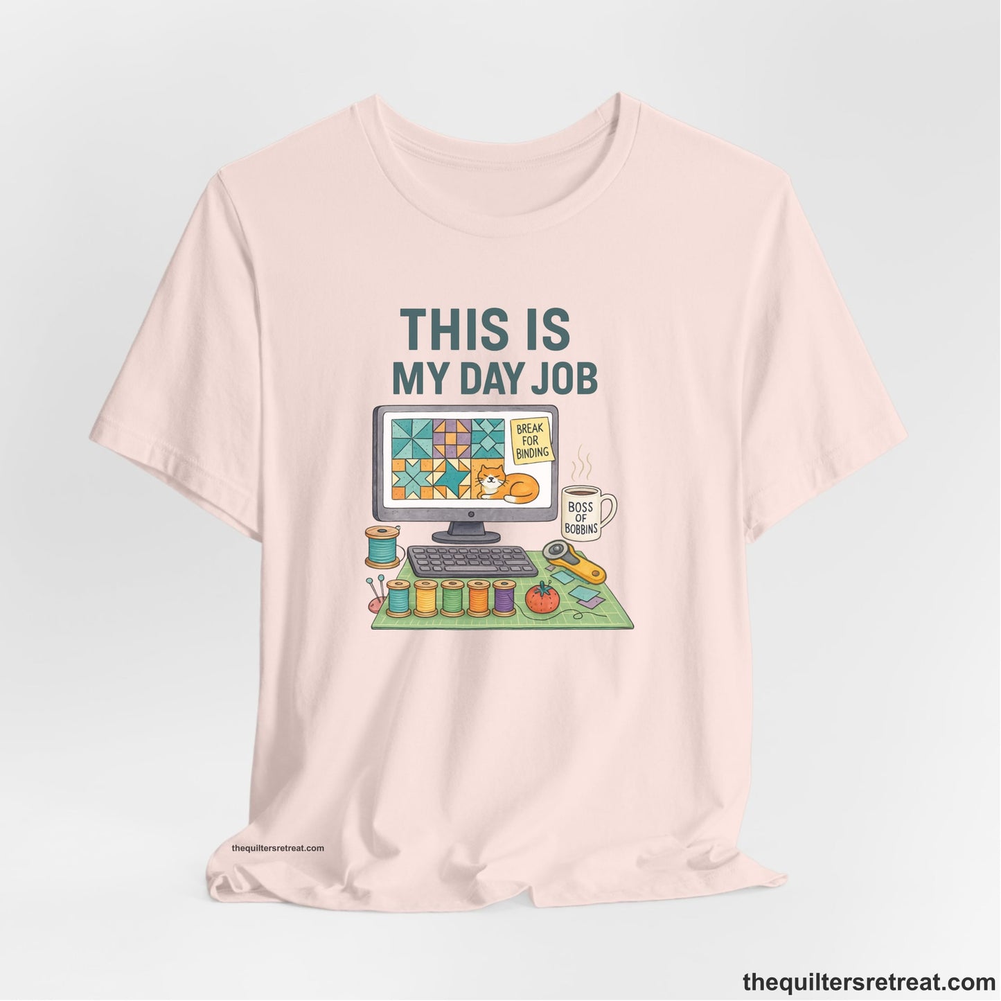 A Soft Pink Short Sleeve T-Shirt with a computer quilt design, cat illustration, "THIS IS MY DAY JOB" text with sewing tools, playful style