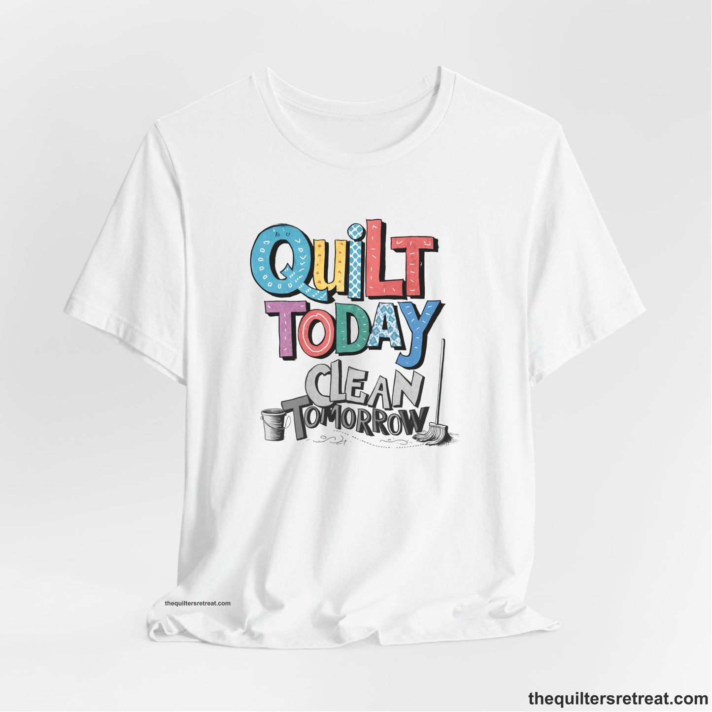 A White Short Sleeve T-Shirt with a playful "Quilt Today Clean Tomorrow" text with colorful patterns and cleaning tools illustration