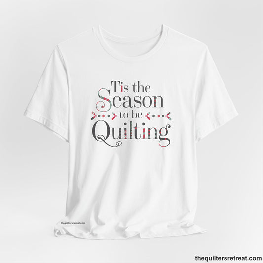A White Short Sleeve T-Shirt with a tis the season to be quilting text with festive patchwork pattern in a cheerful style