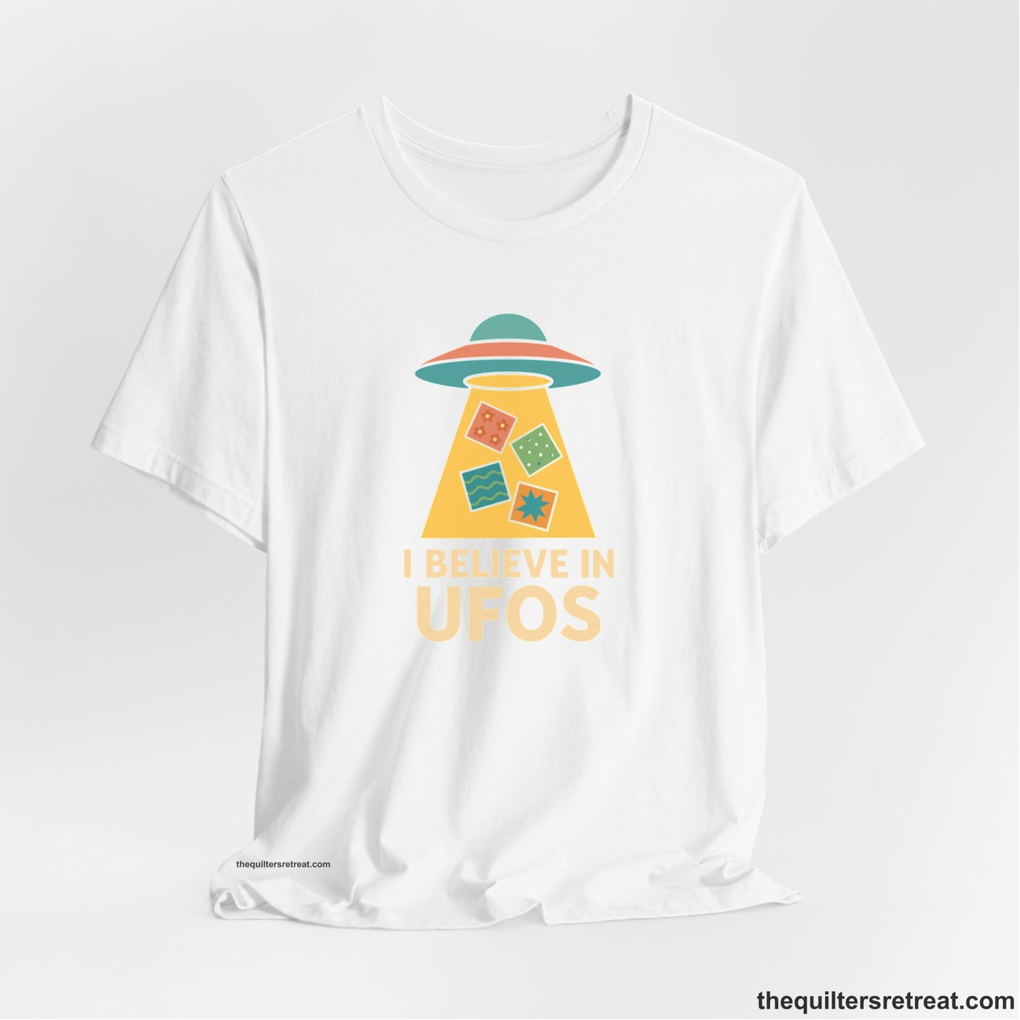 A White Short Sleeve T-Shirt with a colorful UFO with quilt patterns and bold "I Believe in UFOs" text in retro style