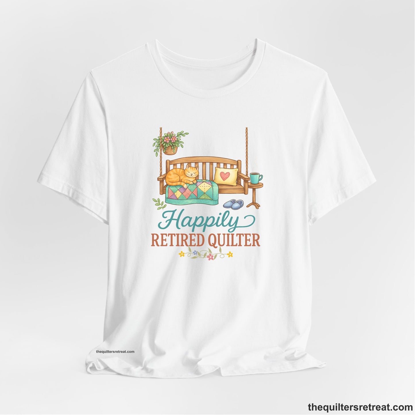 A White Short Sleeve T-Shirt with a hanging bench with cozy cat and quilt, surrounded by plants, "Happily Retired Quilter" text